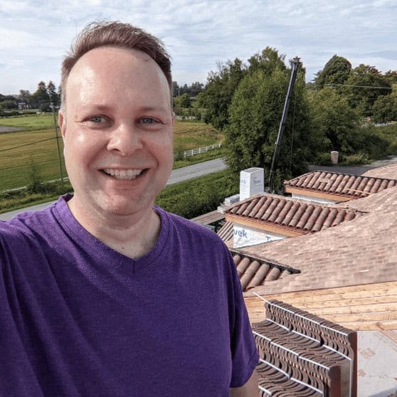 Adam Matthews standing on a roof with clay tiles in the background, representing decades of experience with clay roof tile sourcing and installation.