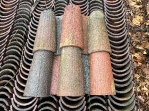 Stack of reclaimed barrel clay roof tiles in red, brown, and moss-weathered finishes, showing natural aging and curved mission profile