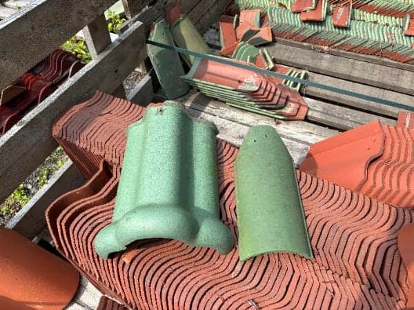 Ludowici Dull Green 206 ridge tile and 102 hip tile displayed on pallets of reclaimed clay roof tiles.