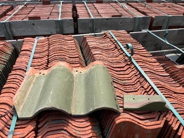 Ludowici 13¼ inch Spanish field tile in Dull Green glaze with matching bird stop, shown on pallets of reclaimed clay roof tiles.
