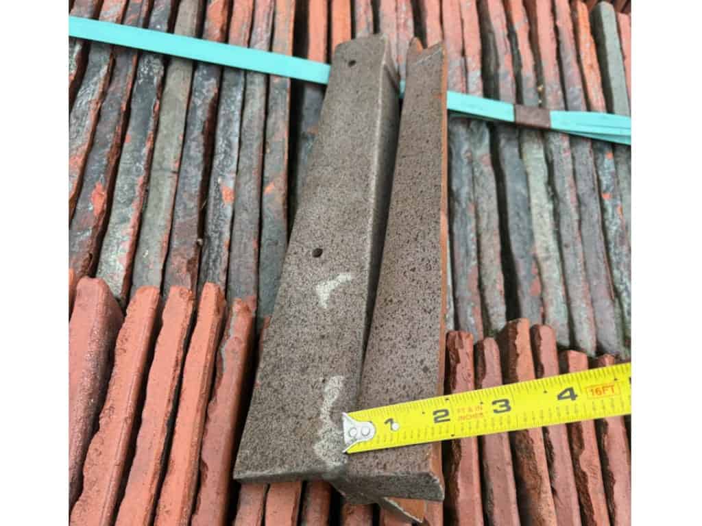 Salvaged Ludowici clay rake cap tile in red terra cotta finish, measured with a tape measure on a pallet of reclaimed tiles.